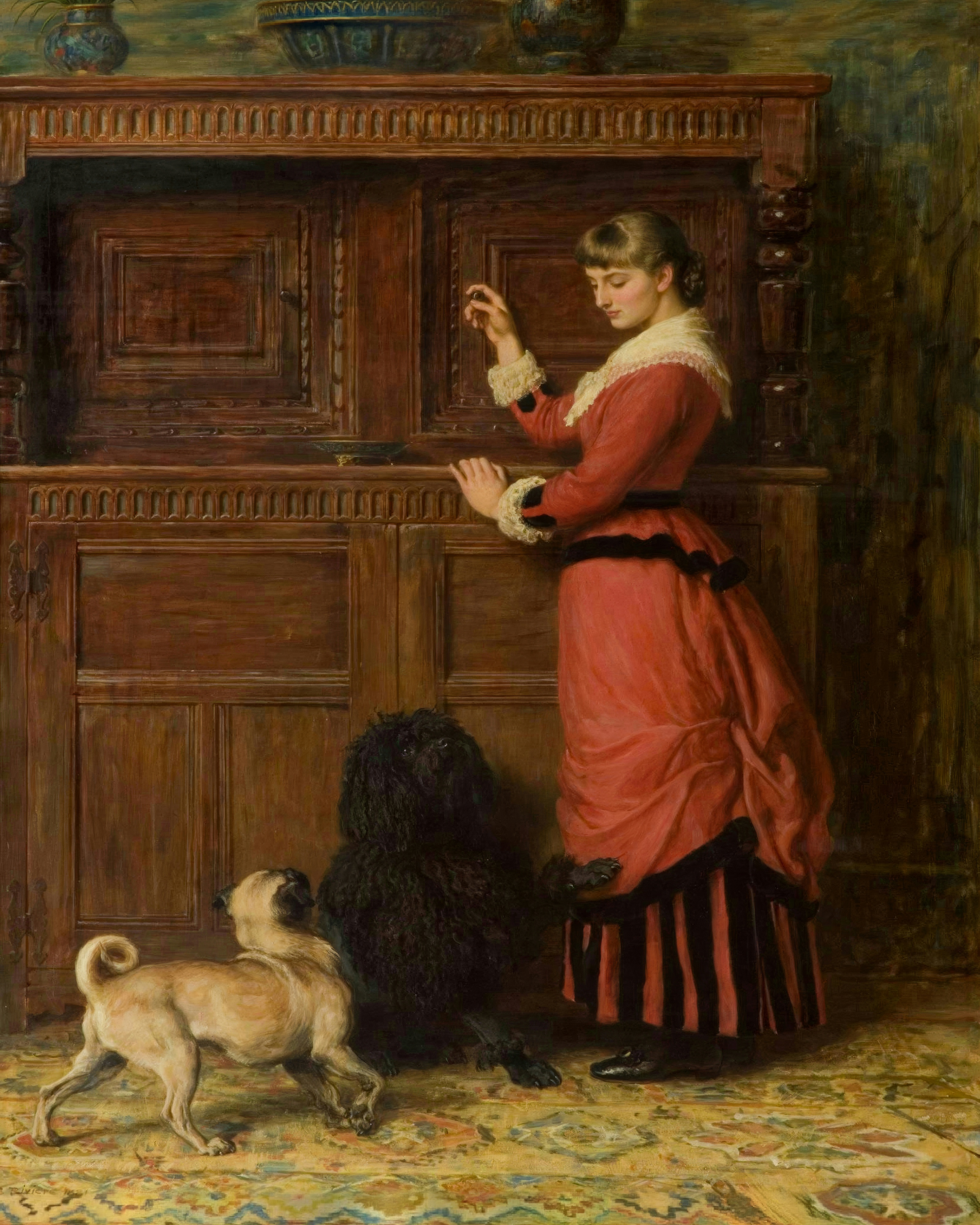A woman in a coral pink gown stands at a large wooden cupboard while two dogs look up eagerly.