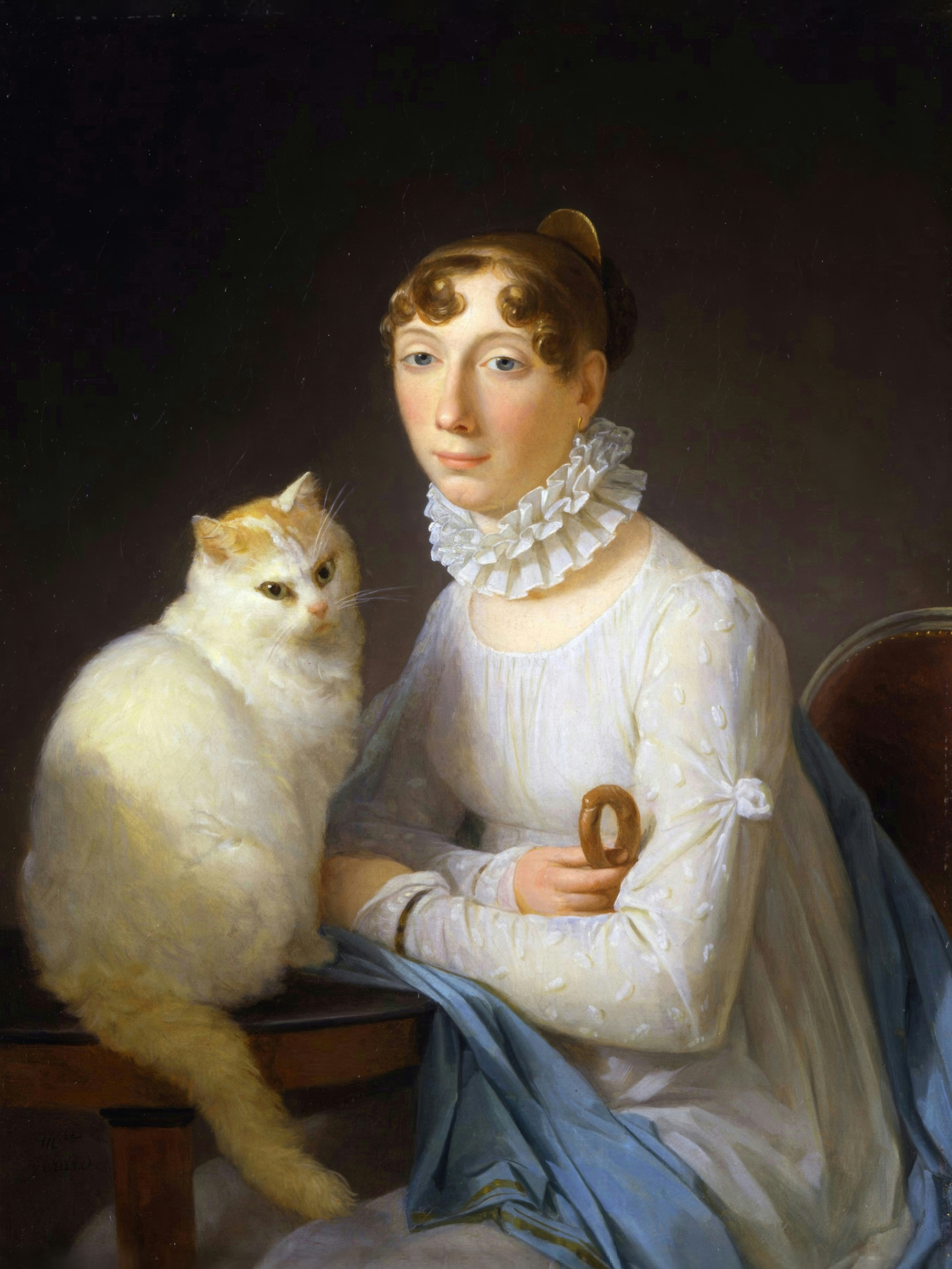 A woman in a white gown and blue shawl sits beside a large fluffy white and orange cat on a polished table.