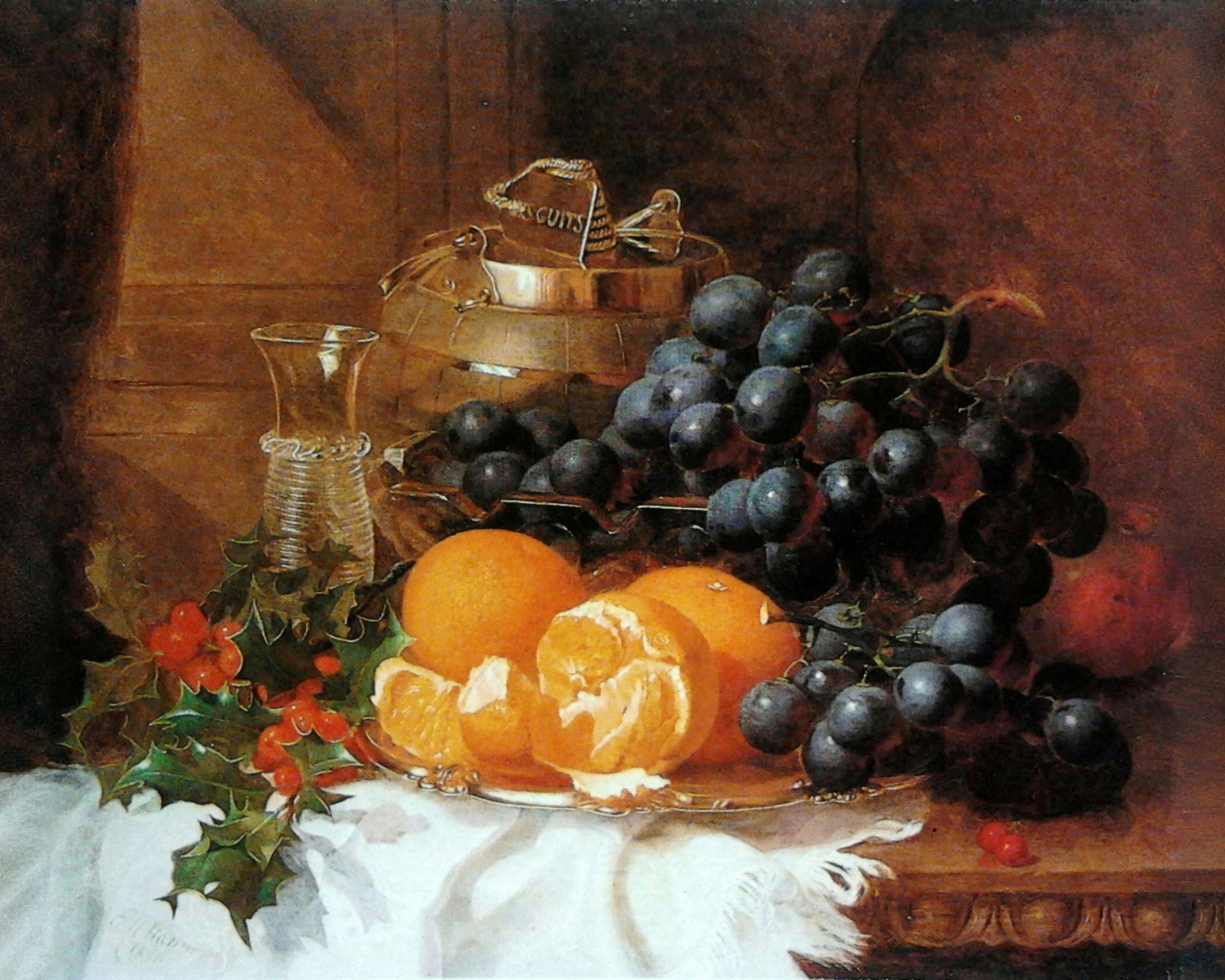 Grapes, oranges and a sprig of red berried holly on a white cloth beside a biscuit barrel.