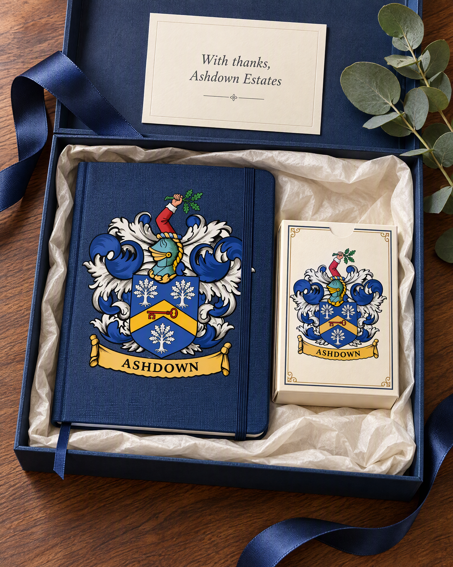 A navy gift box holding a notebook and a deck of playing cards, both with the Ashdown coat of arms, and a card reading With thanks, Ashdown Estates.