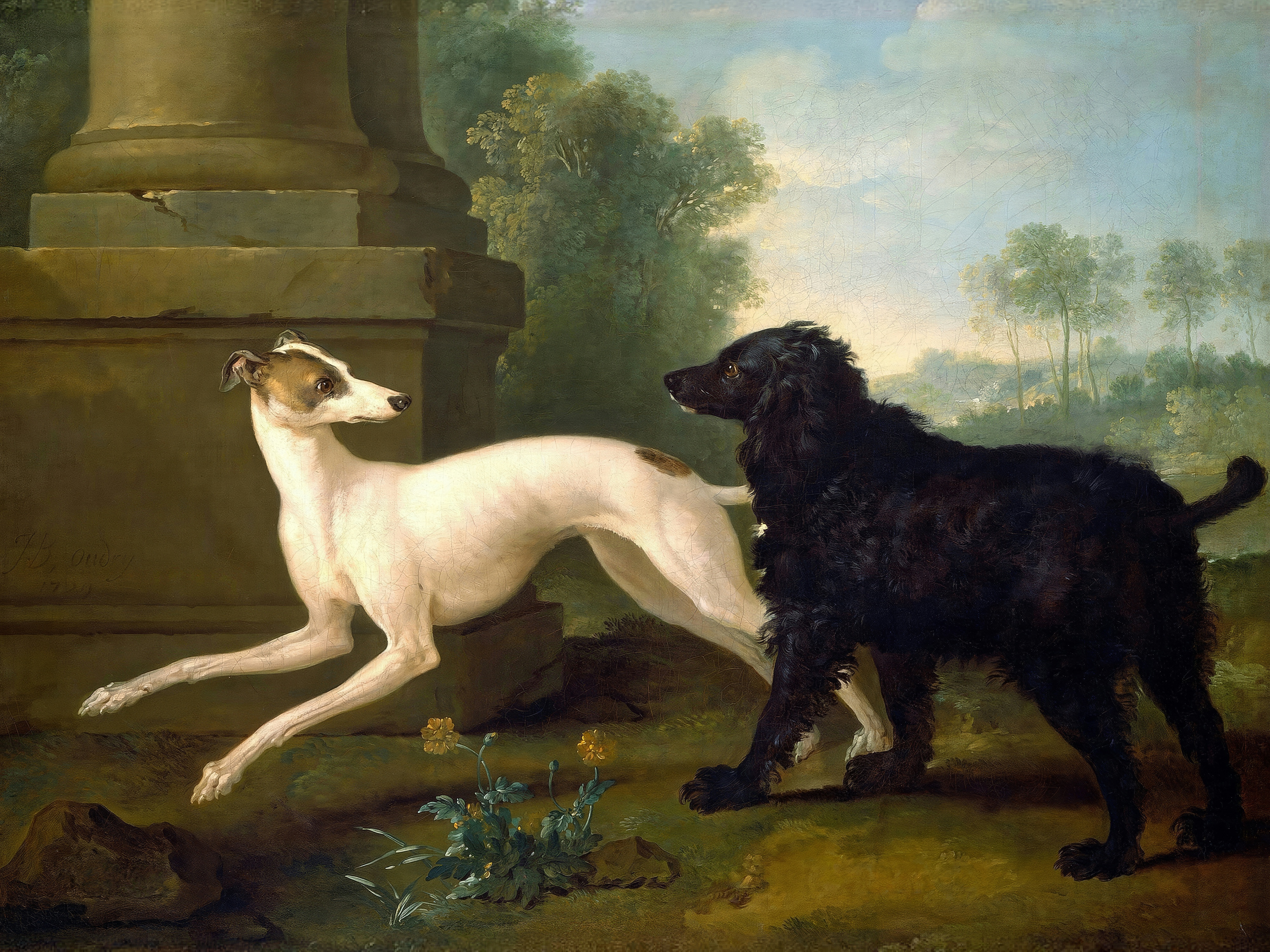 A slender white greyhound and a shaggy black spaniel meet beside a stone pedestal in a leafy park.