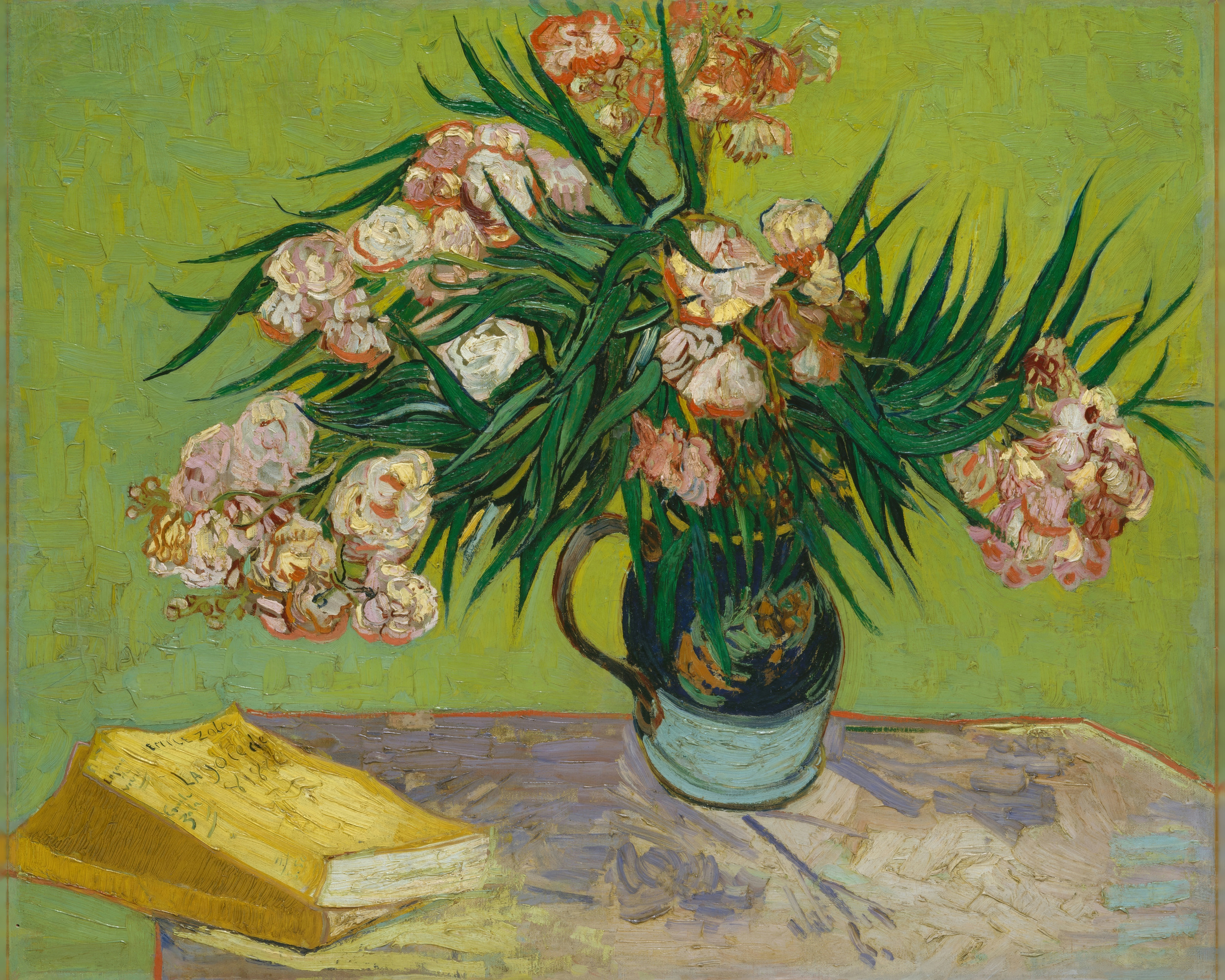 Pink oleanders spill from a green and yellow jug beside two books on a table.