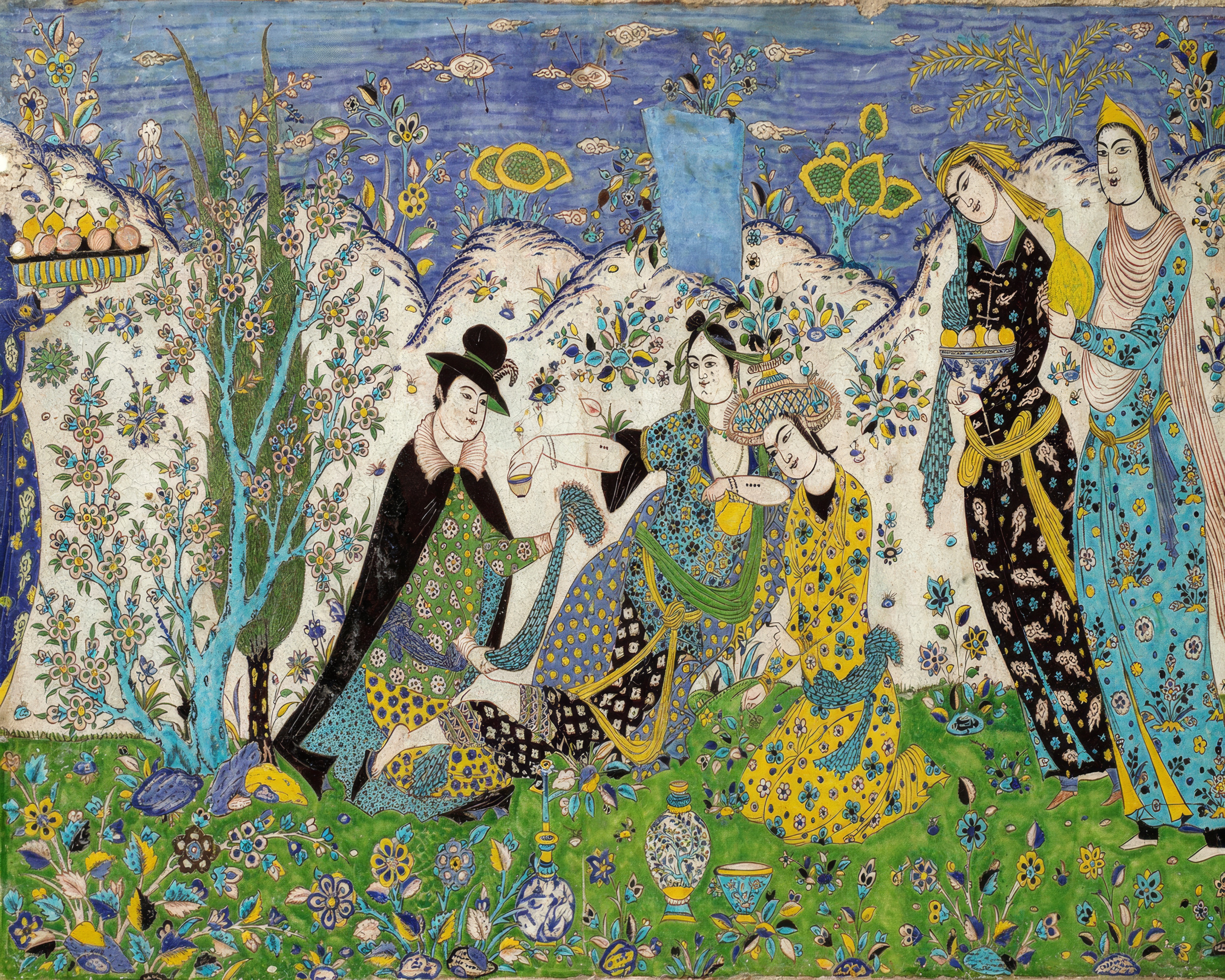 Figures talk under flowering trees in a garden painted on glazed tiles in green, blue and yellow.