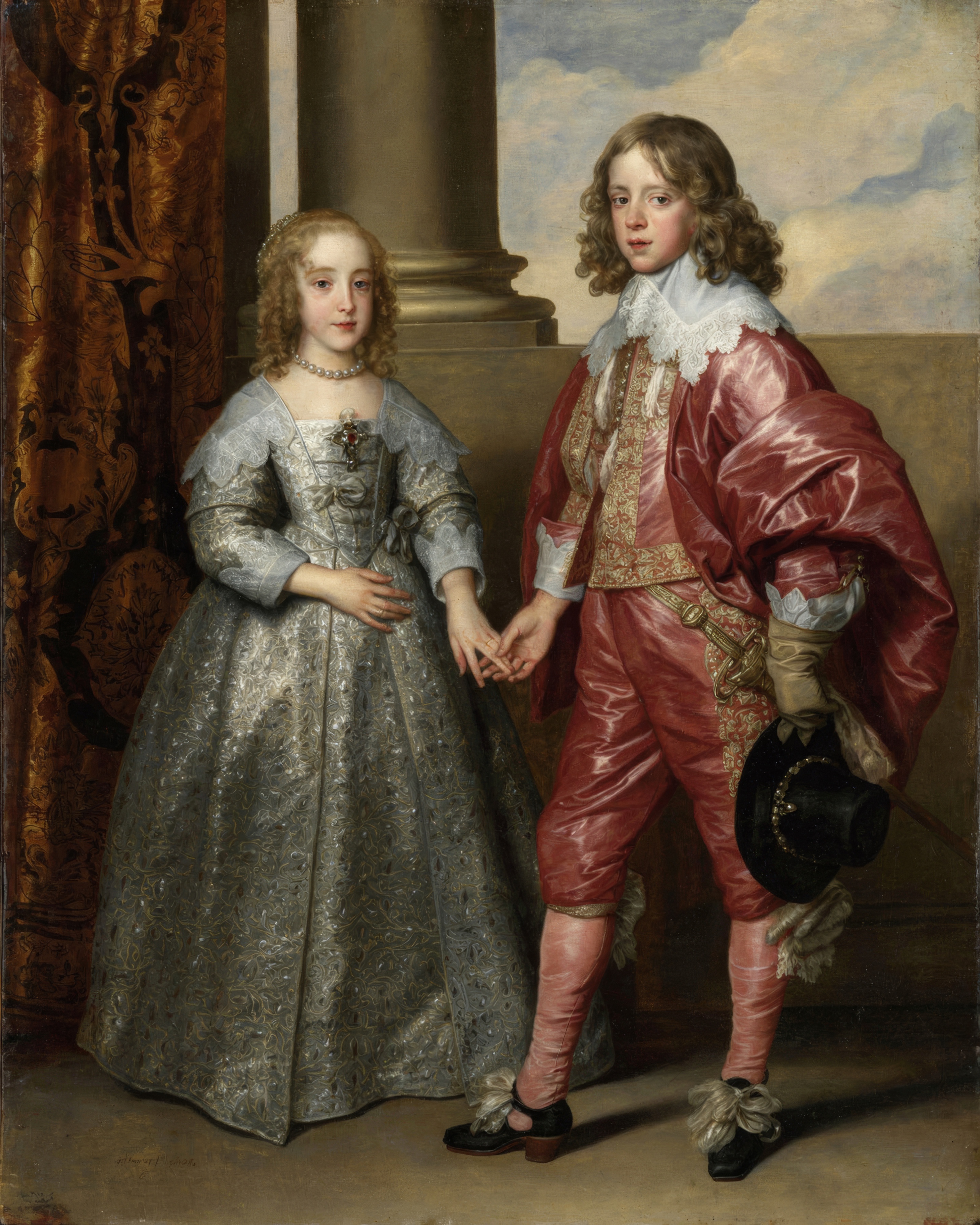 A young prince in red silk holds the hand of a girl in a shimmering silver gown with lace.