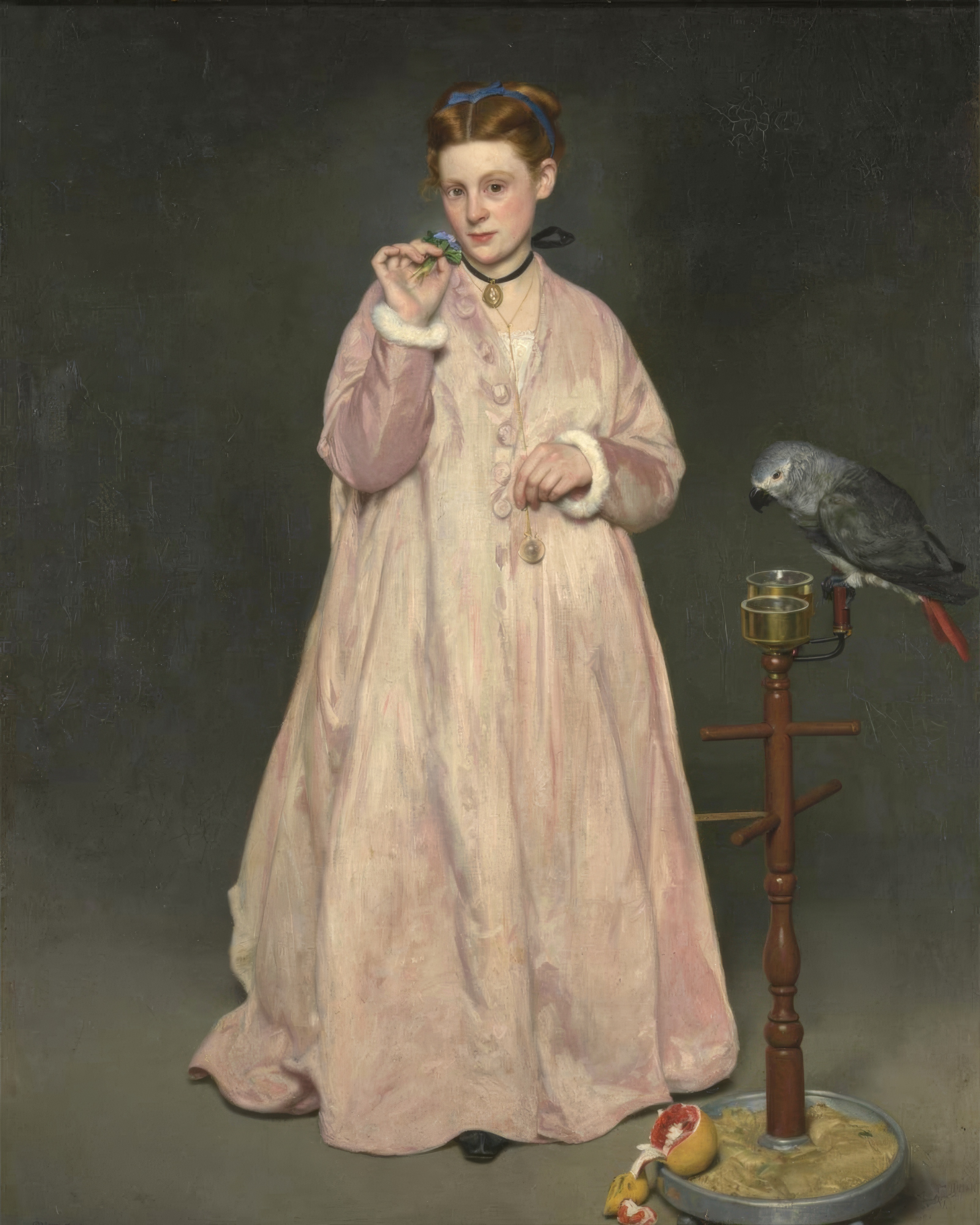A young woman in a long pink dressing gown stands beside a parrot on a perch, holding a violet bouquet.