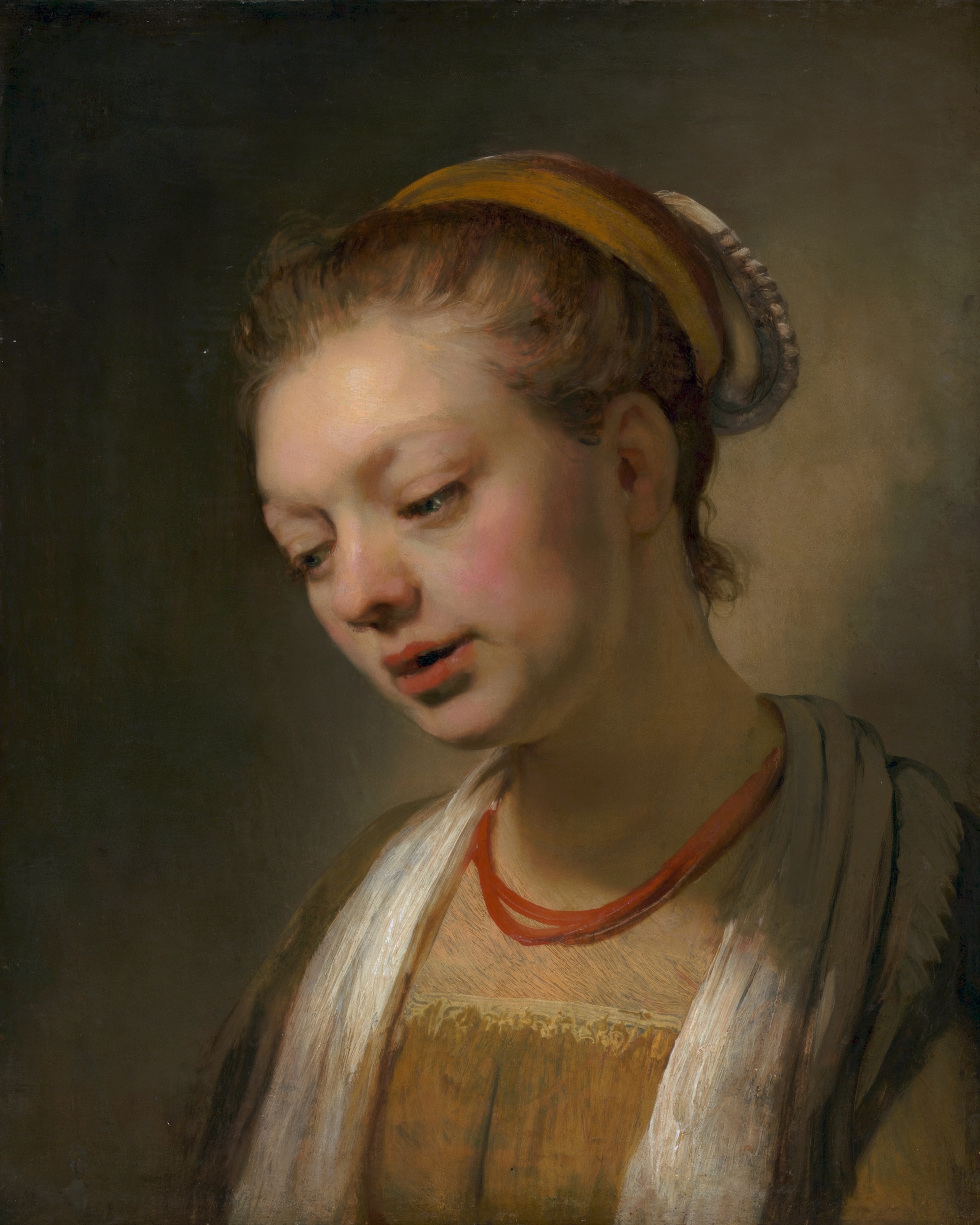 A young woman with a red necklace looks out of deep shadow, lit softly from one side.