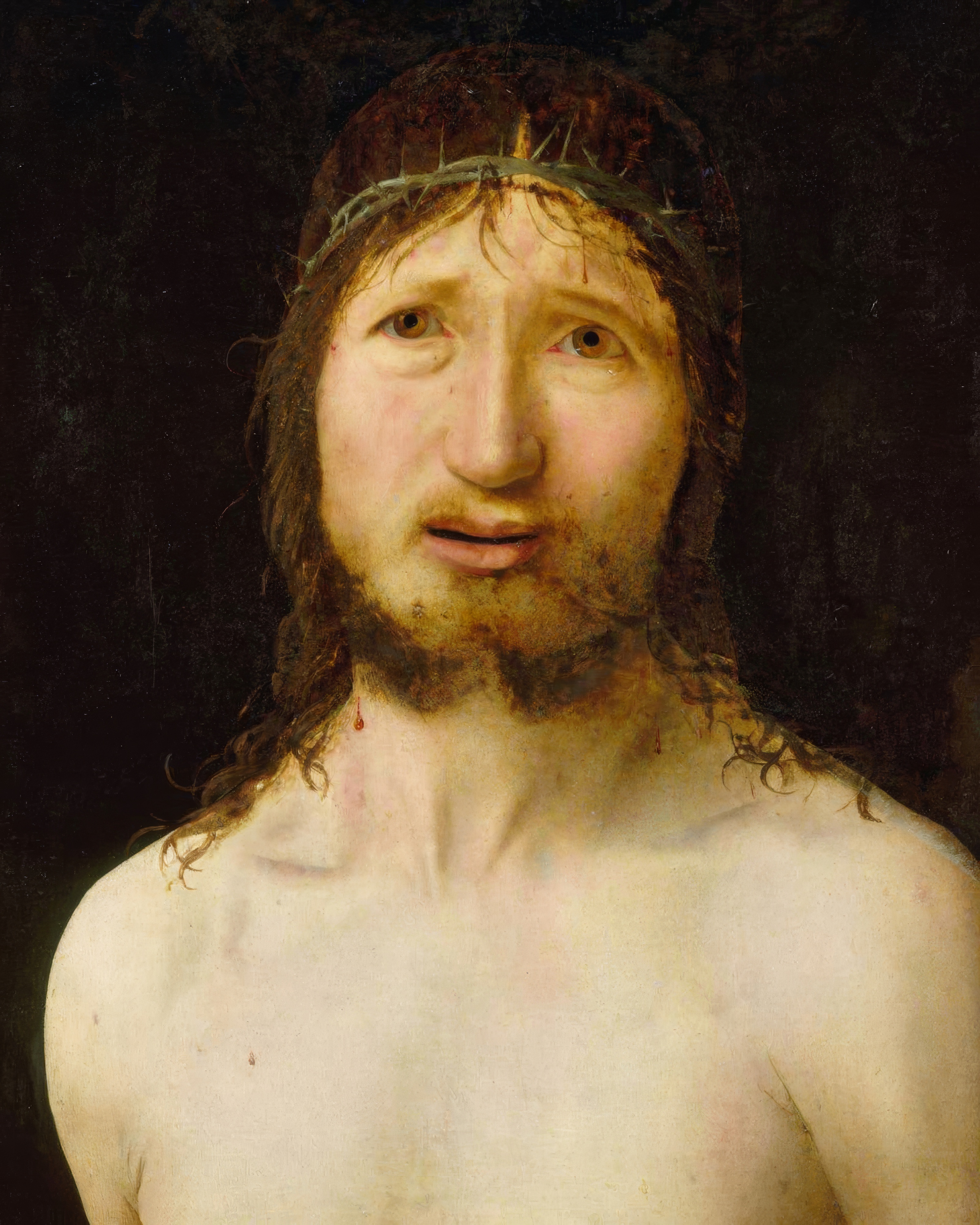 Christ crowned with thorns looks out with tears on his face against a dark background.