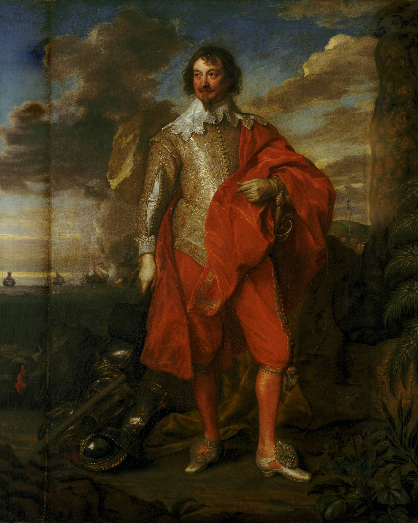The Earl of Warwick in a red costume and armour, hand on hip, stands by the sea with a ship behind.