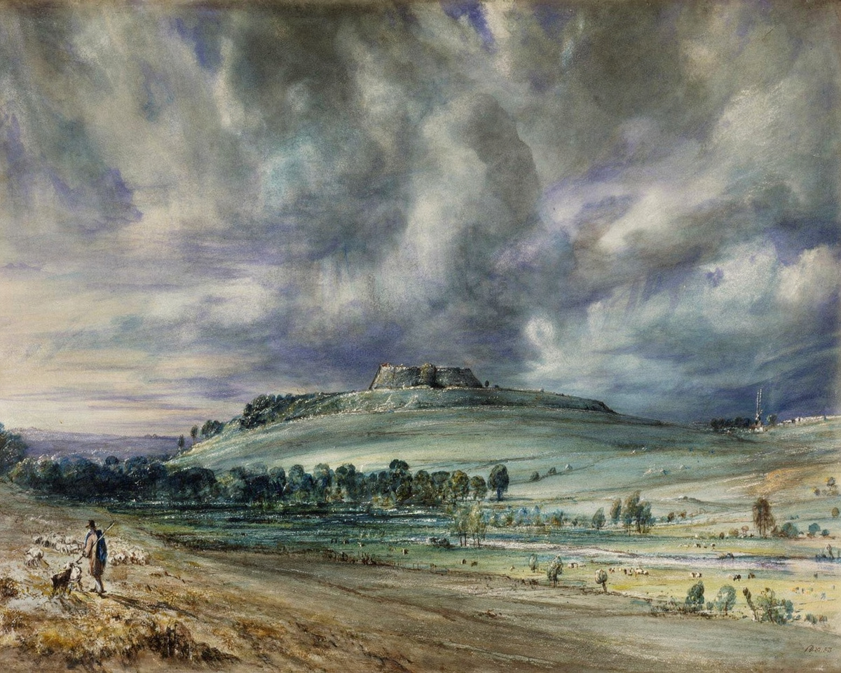 A dark, stormy sky with a rainbow over the grassy mounds of an ancient hill fort.