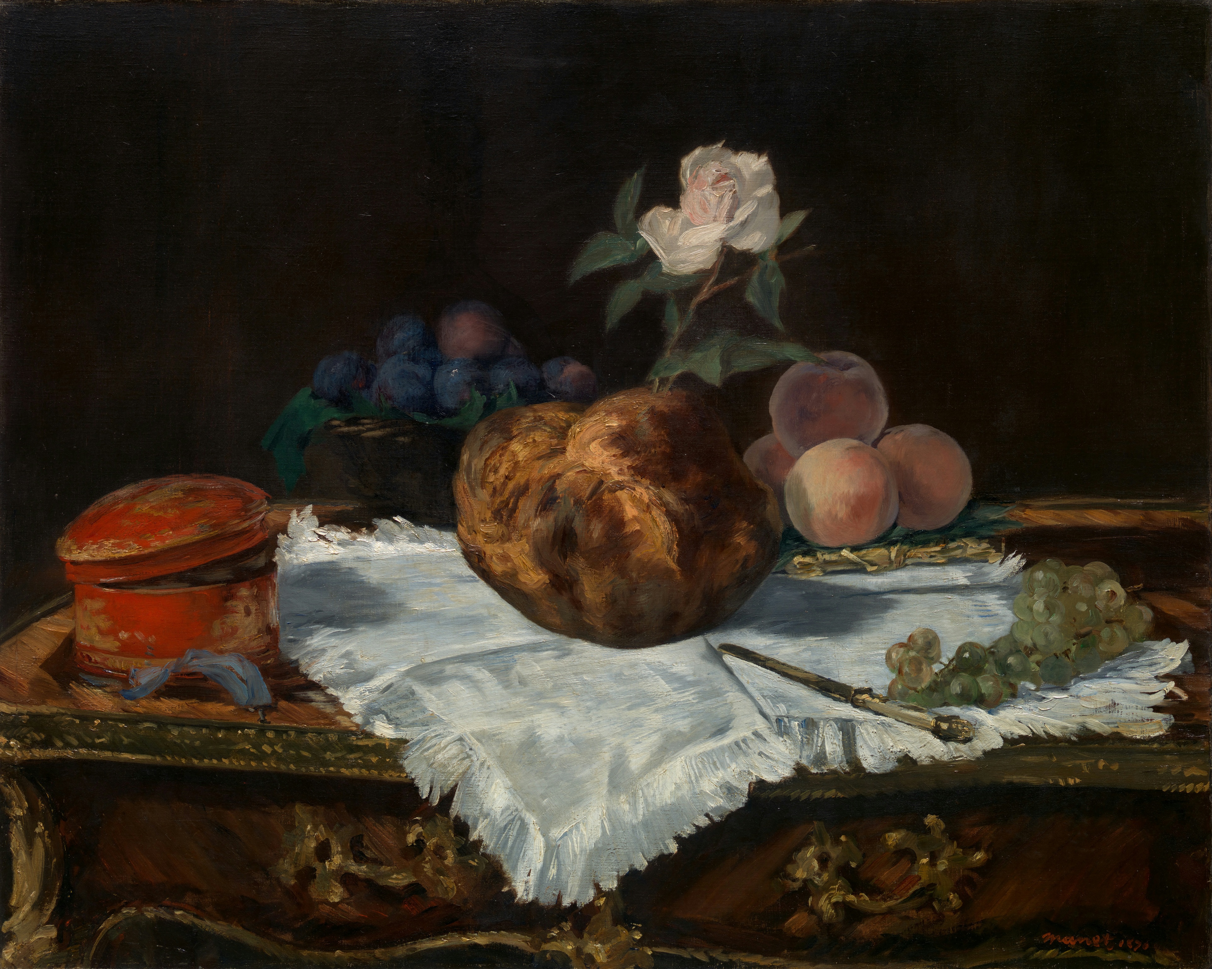 A glazed brioche crowned with a white flower, with fruit at its side.